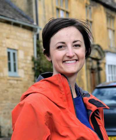 a photo of me in an orange jacket in front of stone buildings in Blockley, England.